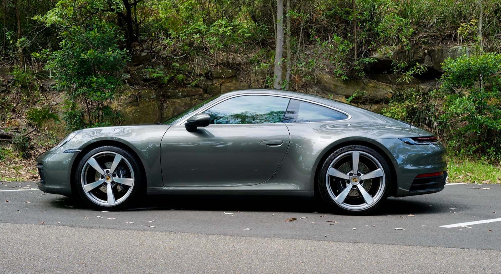 An Aventurine Green Porsche 911 Carrera parked outdoors after regular use.