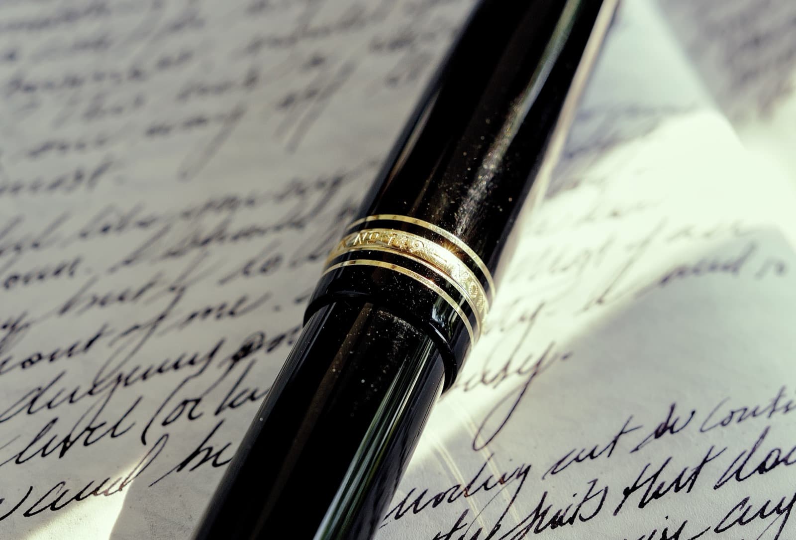 A Montblanc 149 fountain pen resting diagonally across a page of handwritten cursive, its gold cap band catching the light.